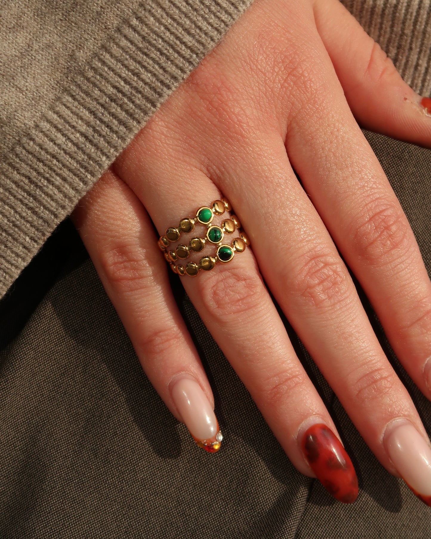 Gouden verstelbare stainless steel ring met drie groene steentjes en verfijnde details, uitgevoerd in een gelaagd design