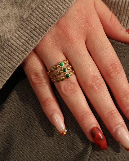 Gouden verstelbare stainless steel ring met drie groene steentjes en verfijnde details, uitgevoerd in een gelaagd design