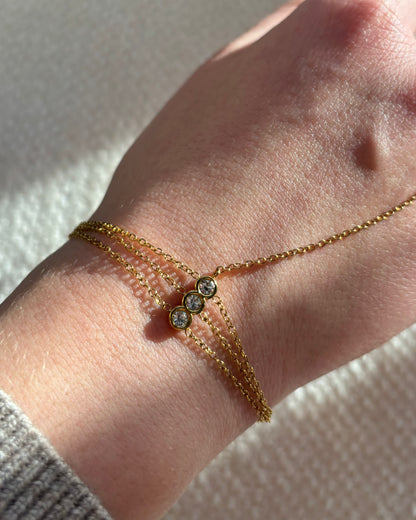 Gouden hand chain met drie fijne armbandbandjes en kleine glinsterende steentjes, verbonden met een ring met één subtiel steentje.