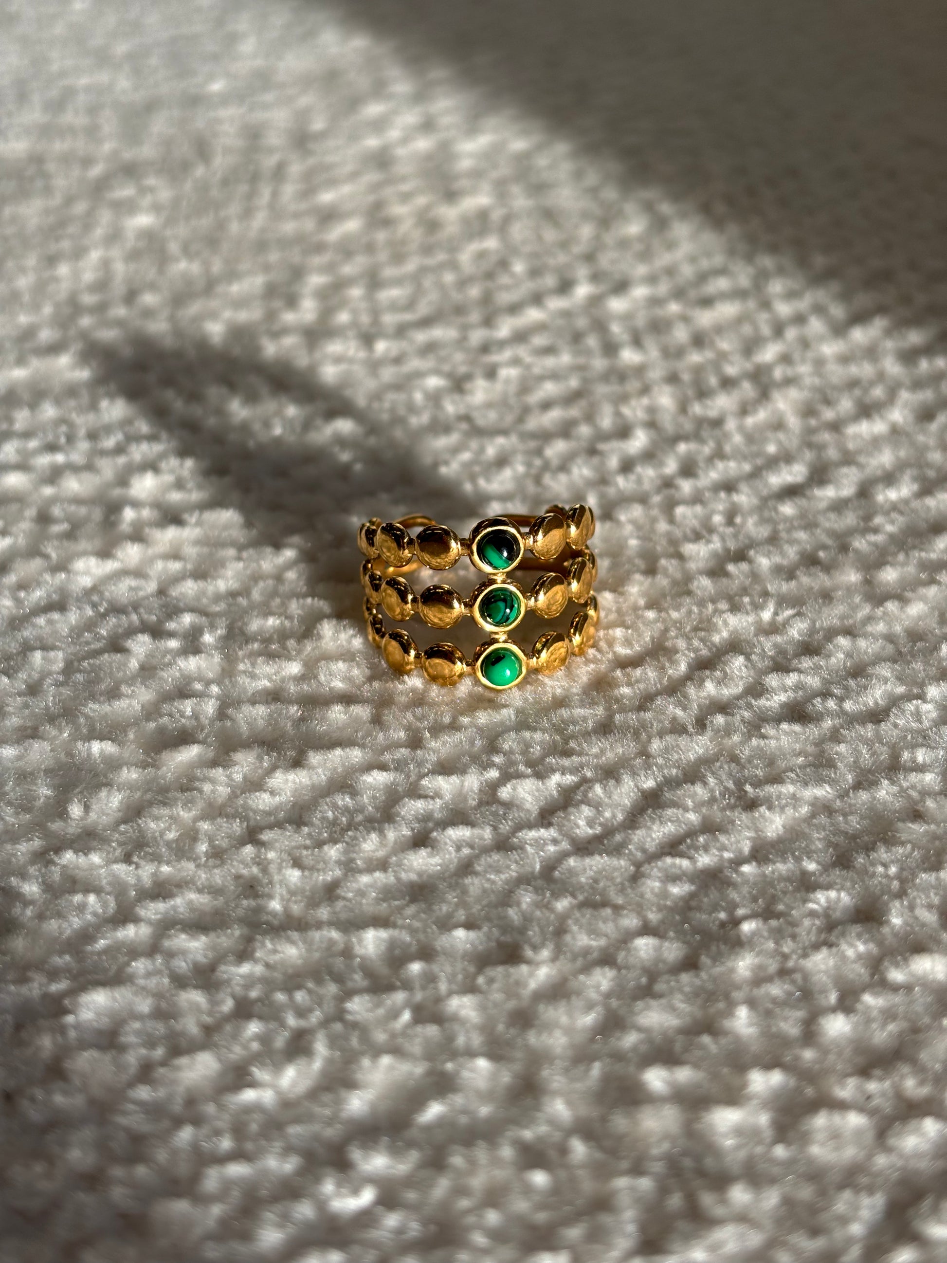 Gouden verstelbare stainless steel ring met drie groene steentjes en verfijnde details, uitgevoerd in een gelaagd design