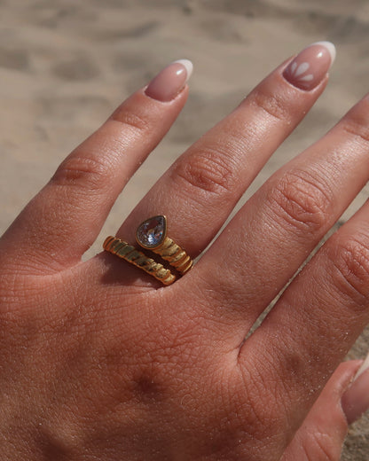 Gouden spiraalvormige ring met reliëf en zilverkleurige druppelvormige steen aan het uiteinde, gemaakt van stainless steel