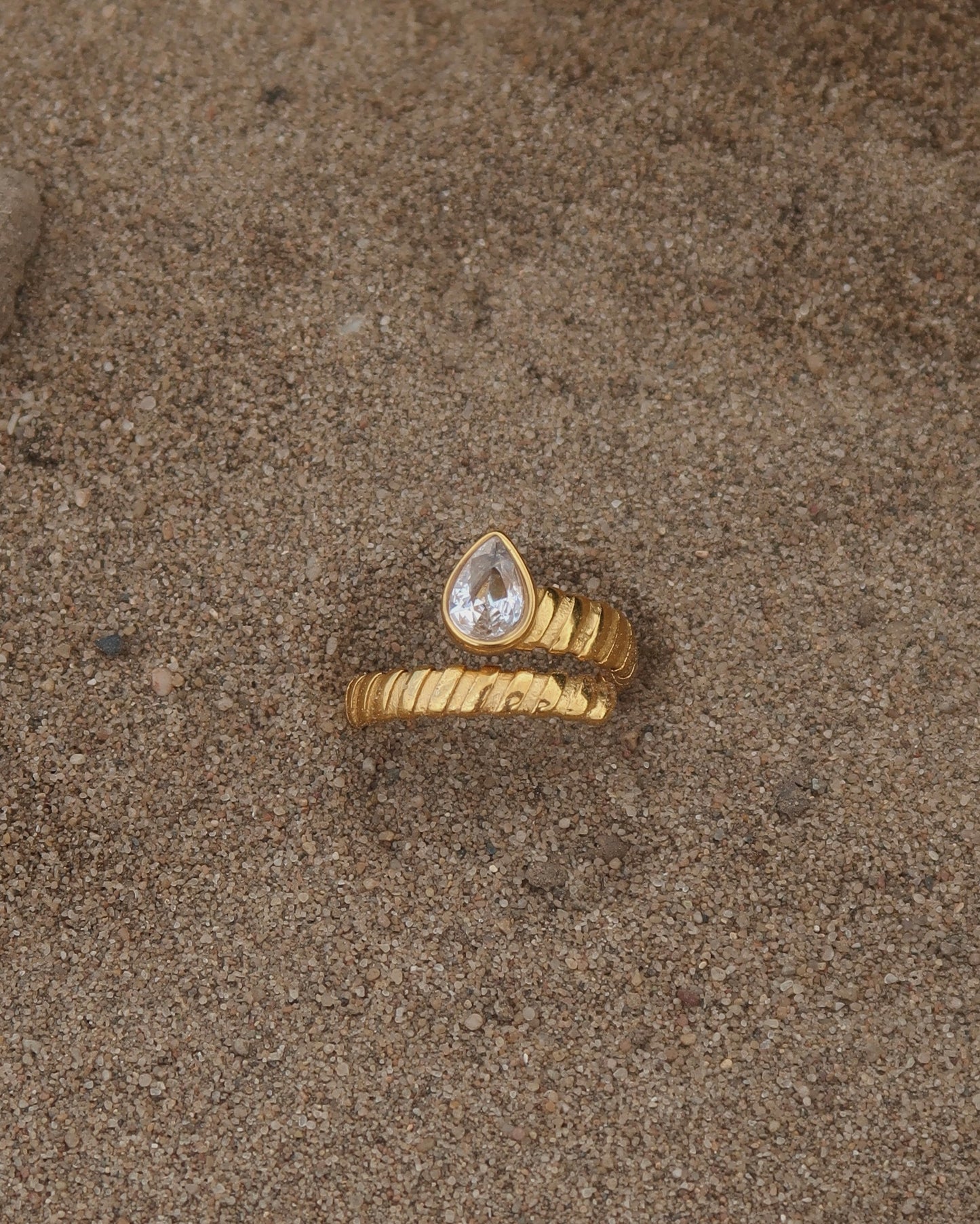 Gouden spiraalvormige ring met reliëf en zilverkleurige druppelvormige steen aan het uiteinde, gemaakt van stainless steel