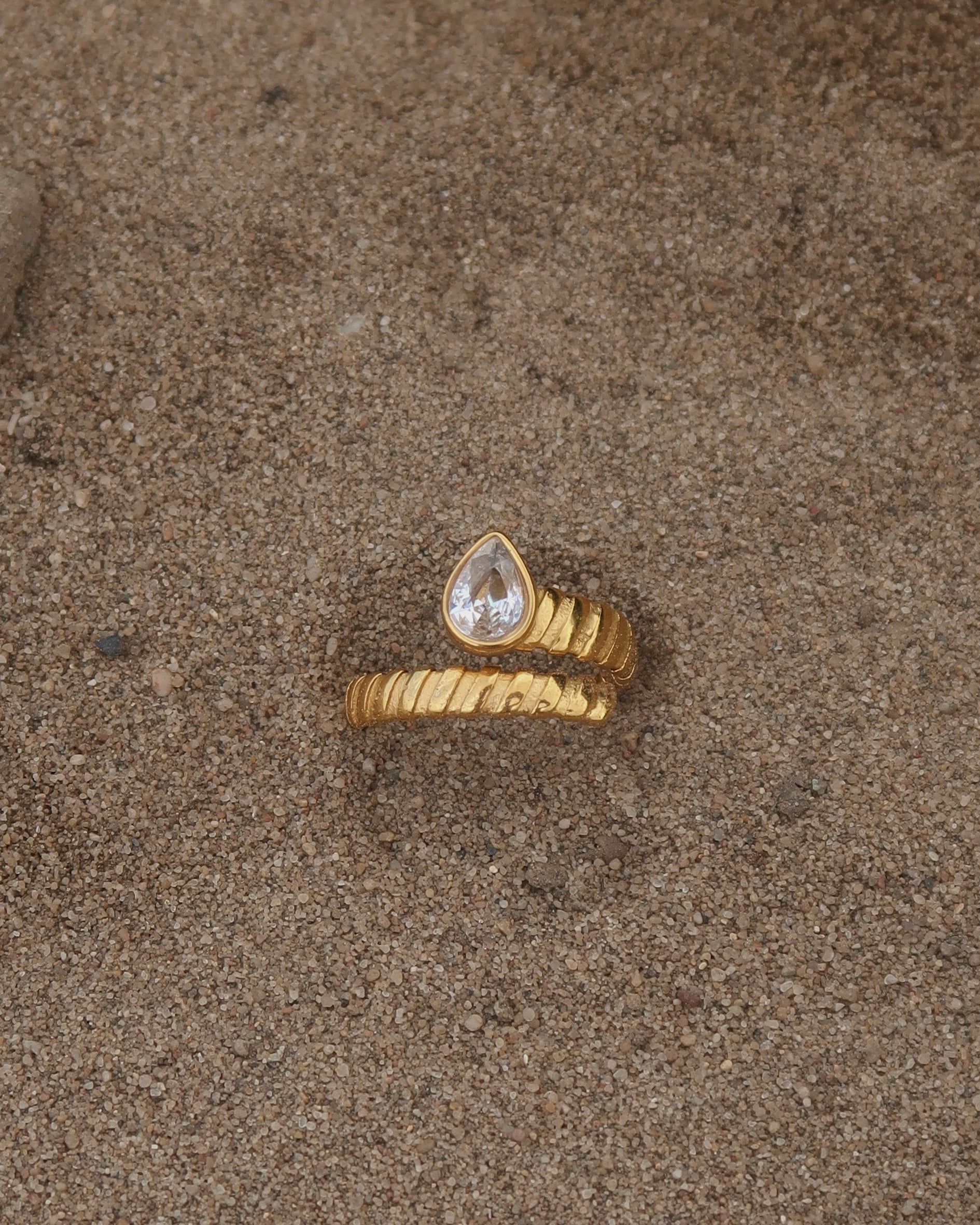 Gouden spiraalvormige ring met reliëf en zilverkleurige druppelvormige steen aan het uiteinde, gemaakt van stainless steel