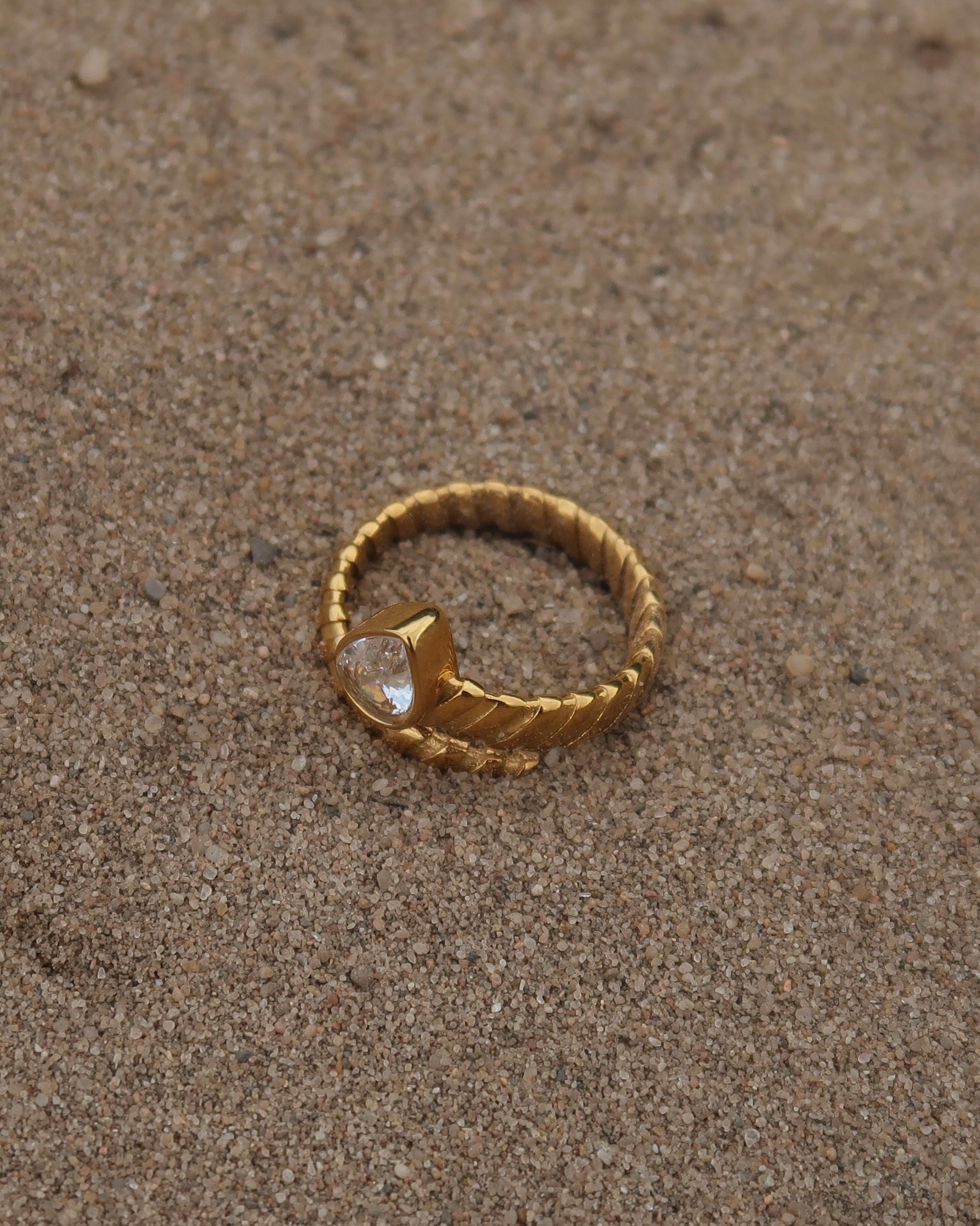 Gouden spiraalvormige ring met reliëf en zilverkleurige druppelvormige steen aan het uiteinde, gemaakt van stainless steel