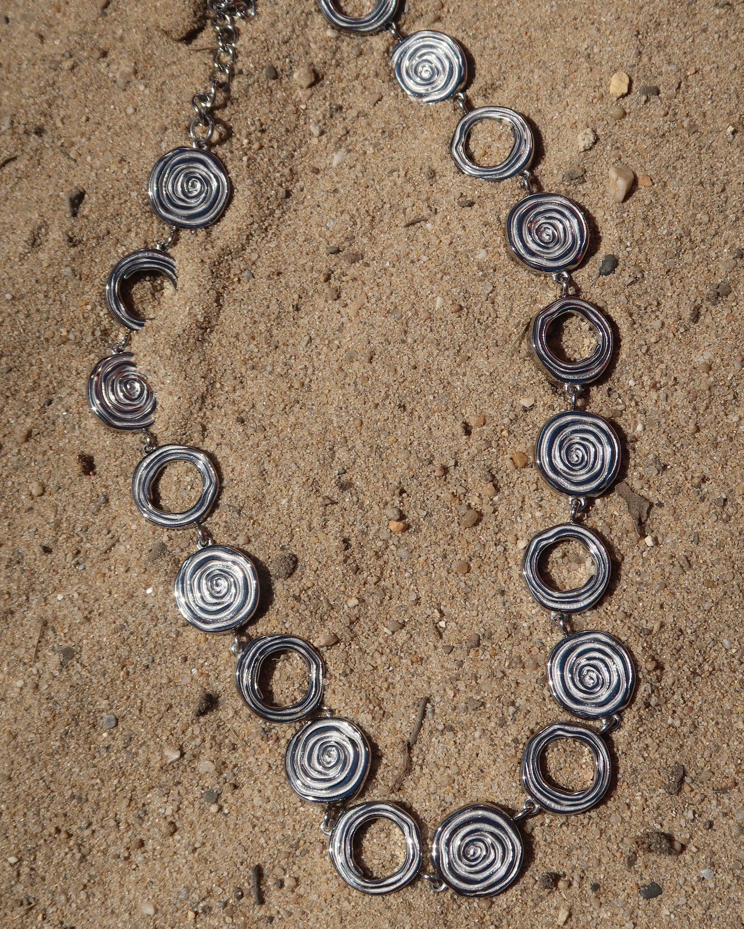 Zilveren statementketting met aaneengeschakelde ronde schelpvormen in verschillende stijlen.