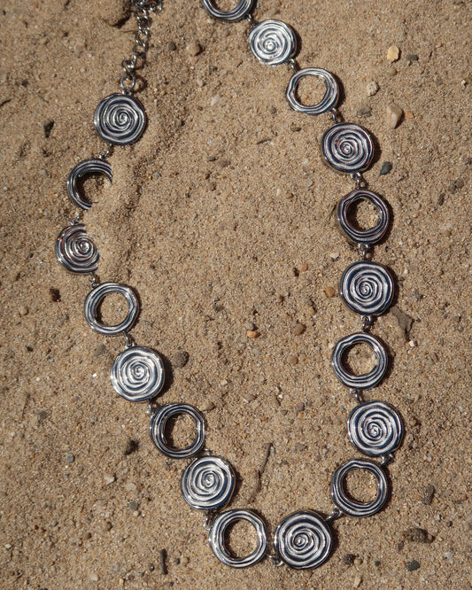 Zilveren statementketting met aaneengeschakelde ronde schelpvormen in verschillende stijlen.