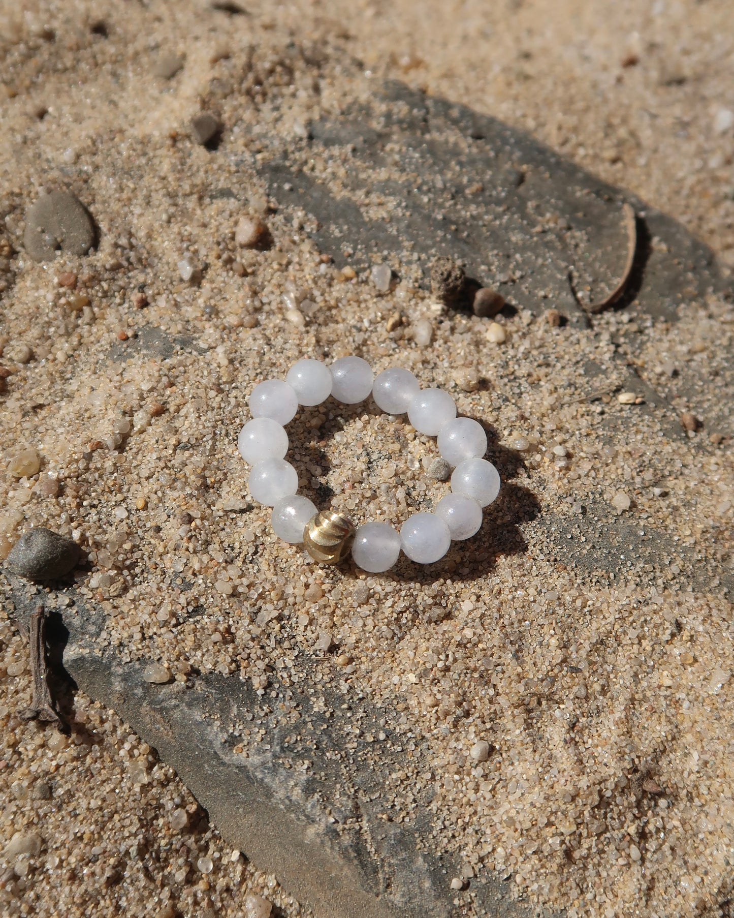 Witte elastische ring met kleine bolletjes en een centraal goudkleurig bolletje, perfect om te combineren met andere ringen