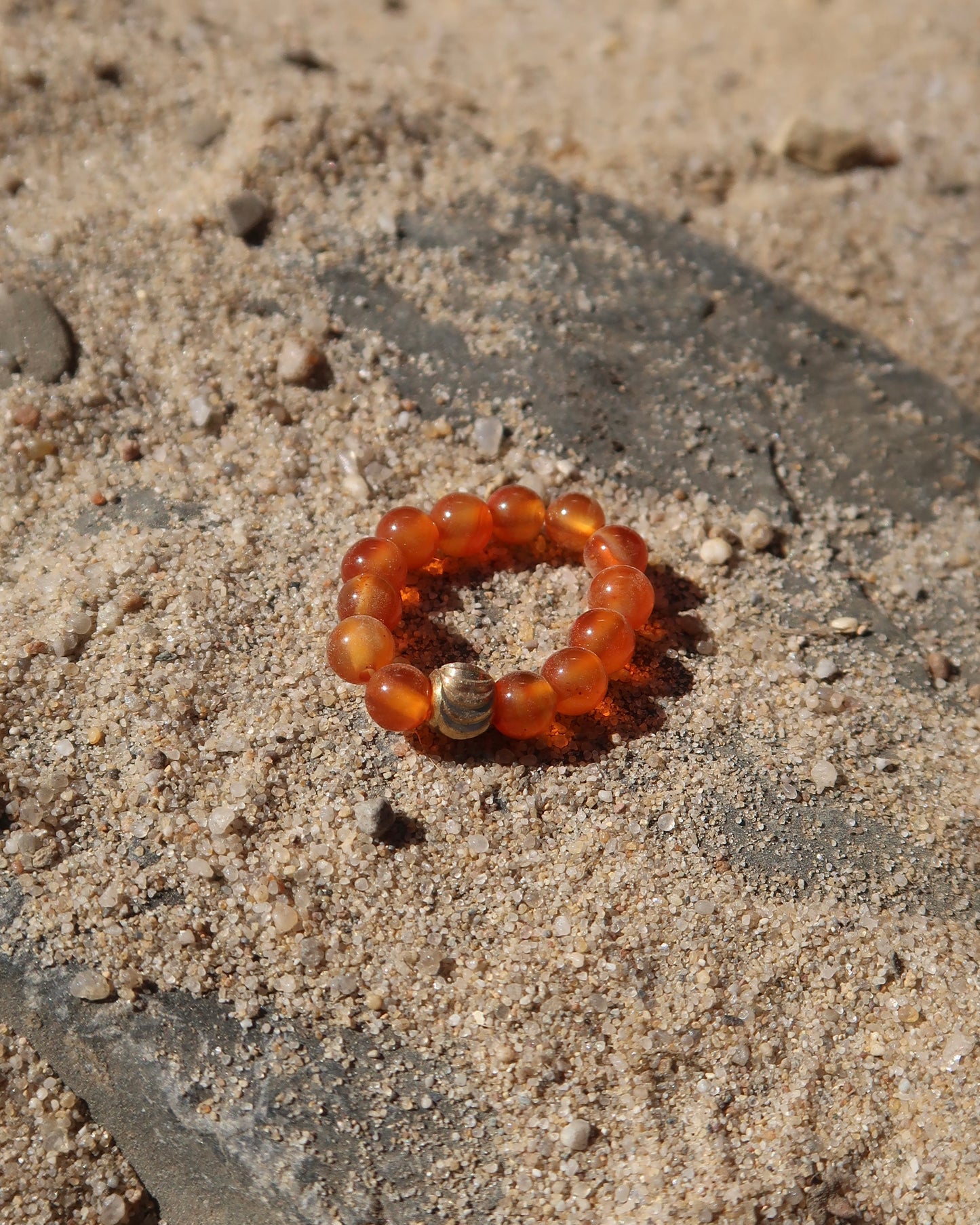 Oranje elastische ring met kleine bolletjes en een centraal goudkleurig bolletje, perfect om te combineren met andere ringen