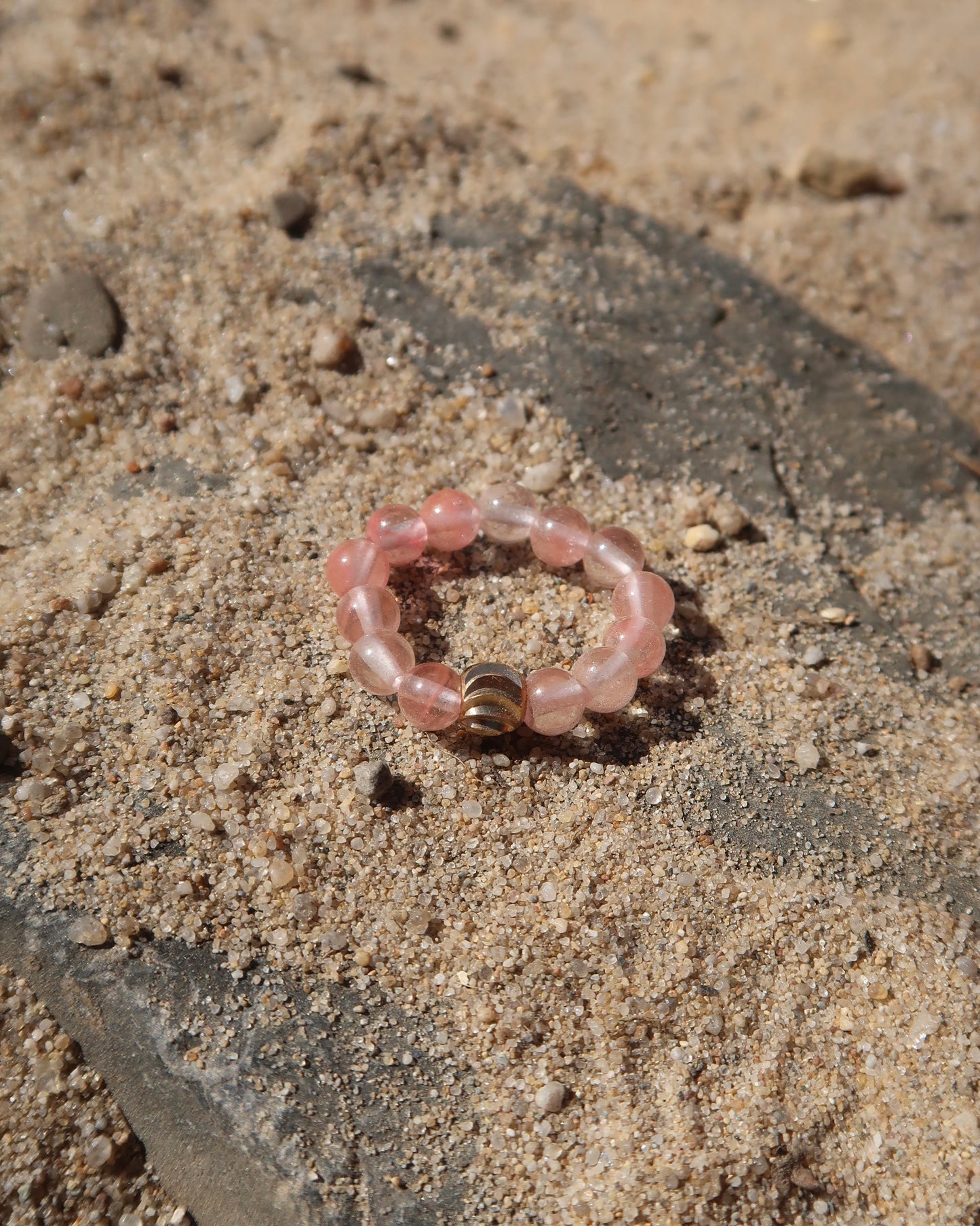 Roze elastische ring met kleine bolletjes en een centraal goudkleurig bolletje, perfect om te combineren met andere ringen