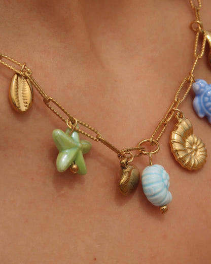 Gouden ketting met zeven bedels, waaronder gouden schelpen, een blauwe schildpad, een blauwe schelp en een groene zeester. De bedels vormen een speelse combinatie van goud met frisse blauw- en groentinten.