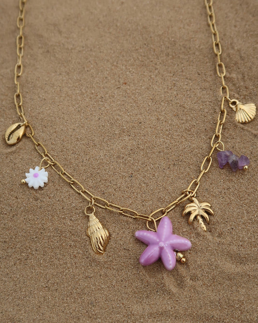 Gouden ketting met zeven bedels, waaronder gouden schelpjes, een paarse zeester, een wit bloemetje met paars hart, paarse steentjes en een gouden palmboom. De ketting heeft een speelse uitstraling met paarse accenten en zomerse details.