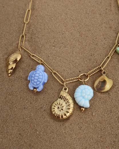 Gouden ketting met zeven bedels, waaronder gouden schelpen, een blauwe schildpad, een blauwe schelp en een groene zeester. De bedels vormen een speelse combinatie van goud met frisse blauw- en groentinten.